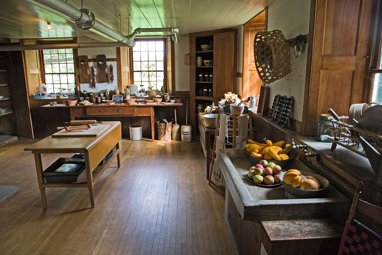 A historic Shaker kitchen with plain wooden worktables, cupboards and shelves